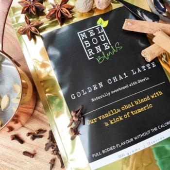 Turmeric Chai Latte packed in 200gr gold bag with black label position on timber board decorated with spices and flower