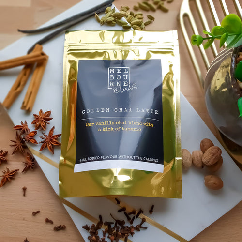 Turmeric Chai Latte packed in 200gr gold bag with black label position on timber board decorated with spices and flower