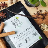 Vanilla Chai Latte, packed in 200gr black bag with white label position on timber board decorated with spices and flower